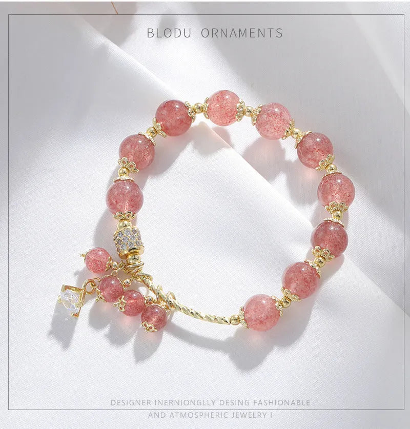 Close-up of a women's pink bracelet with a heart-shaped strawberry quartz crystal and small pearl accents on the band.