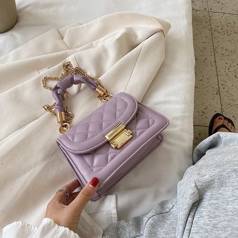 Purple soft PU leather small square shoulder bag with a long strap on a table.
