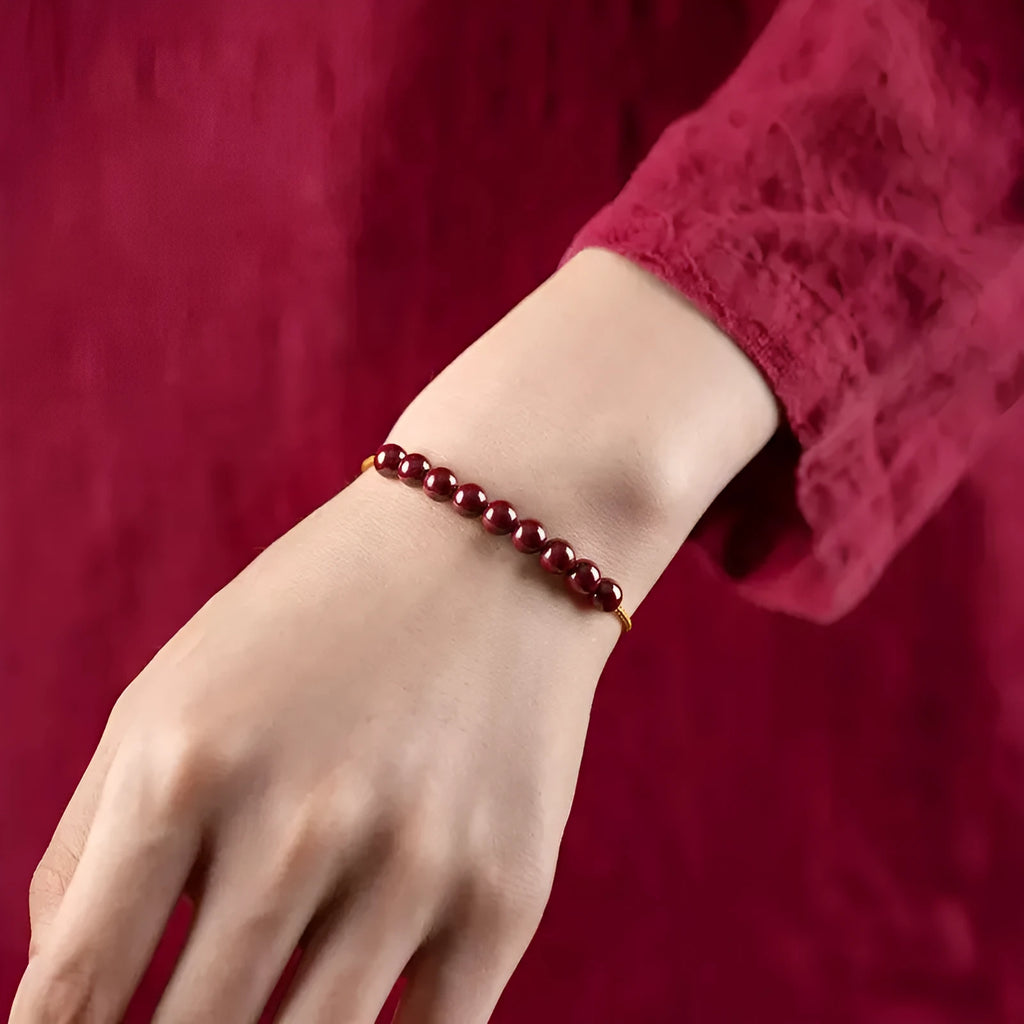 Close-up of a geometric design bracelet made from dark red cinnabar and Hetian jade on a wrist.