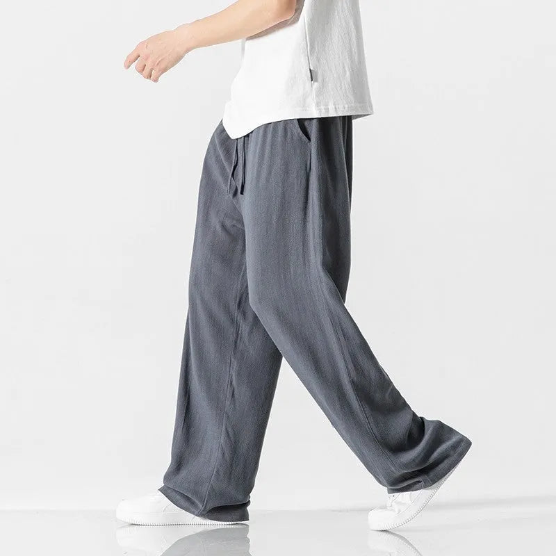 Men's beige linen-style trousers with a loose straight-leg fit and drawstring waist, laid flat.