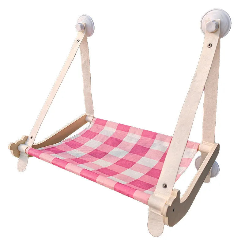 Wooden frame cat hammock with linen mat attached to a window via suction cups, shown in pink colour.