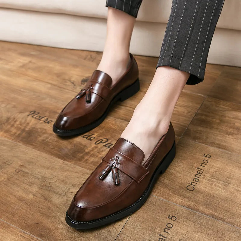 Men's black tassel slip-on loafers with a pointed toe and rubber sole on a white background.