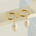 A pair of geometric drop earrings with a gold metal frame and a central freshwater pearl.