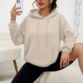 Woman wearing a loose grey sweatshirt with a front pocket and drawstring hem.