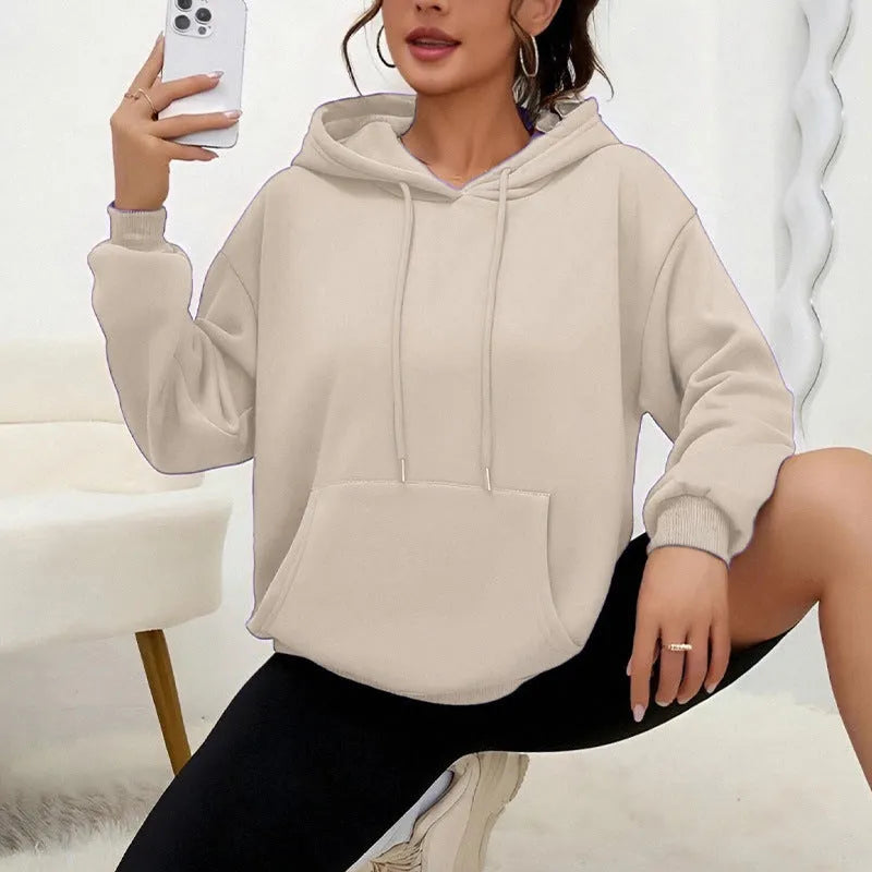 Woman wearing a loose grey sweatshirt with a front pocket and drawstring hem.
