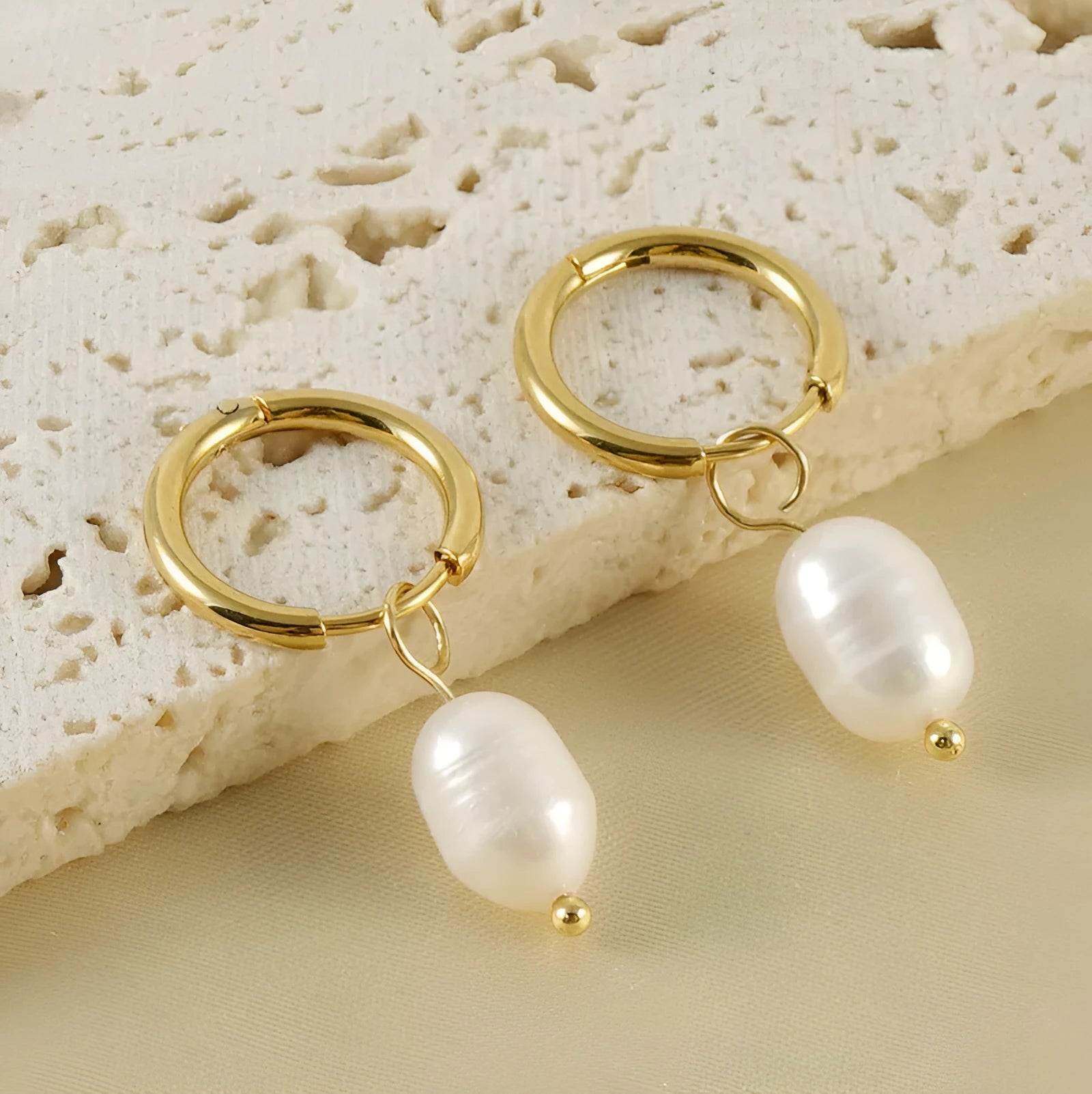 A pair of geometric drop earrings with a gold metal frame and a central freshwater pearl.