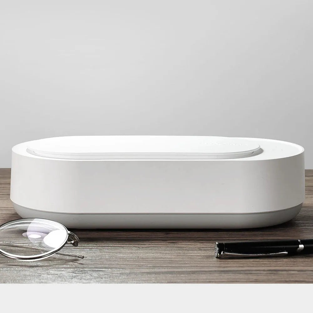 White portable ultrasonic cleaner with touch button next to jewellery and glasses on a table.