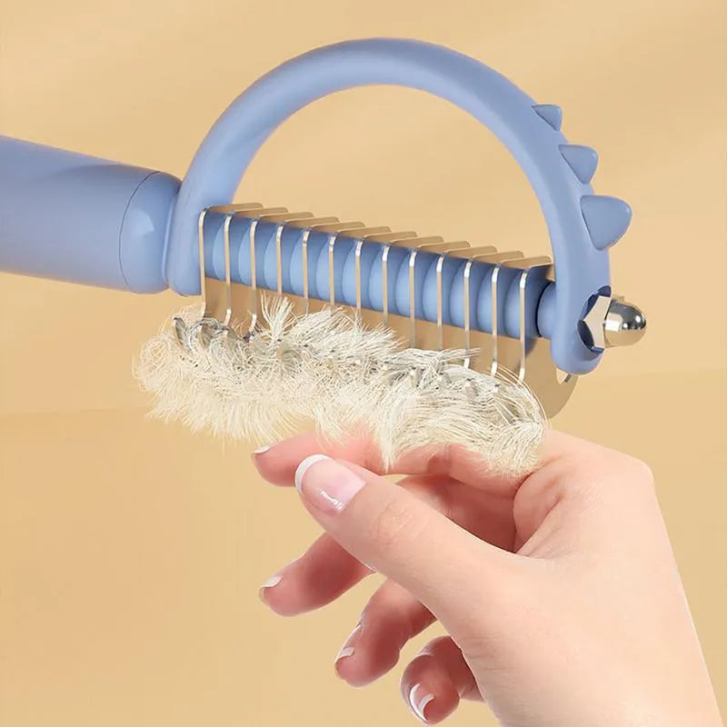 Blue dinosaur-shaped self-cleaning cat brush with stainless steel pins on a white background.