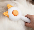 A greenish white and orange cat grooming comb with stainless steel teeth and a self-cleaning button.