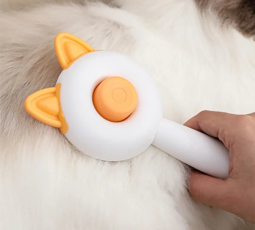 A greenish white and orange cat grooming comb with stainless steel teeth and a self-cleaning button.