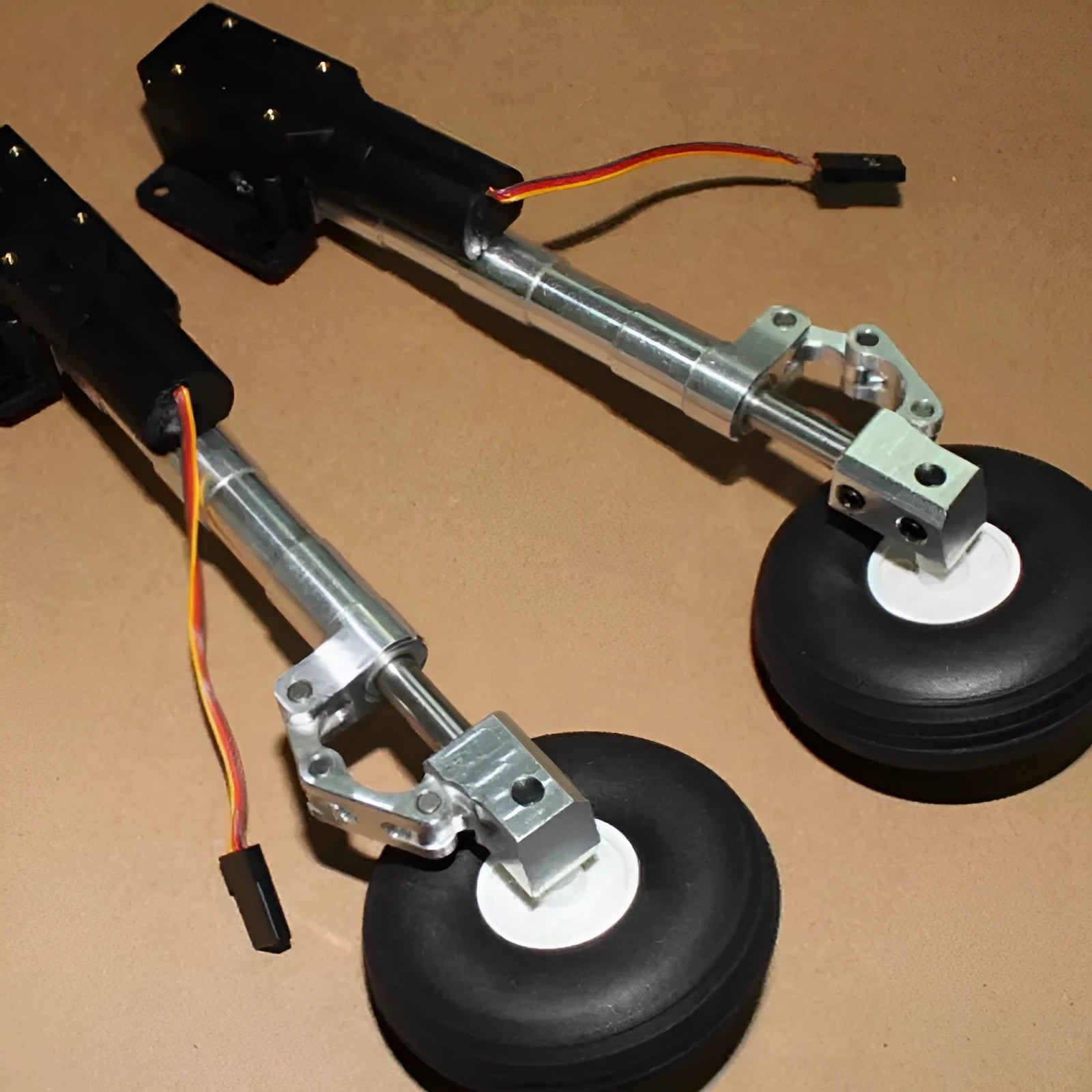 Retractable alloy landing gear with wheels for toy aircraft, shown in inclined kneeling shock-absorbing position.