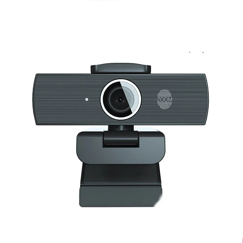 Black USB webcam with magnetic privacy cover on a desk next to a laptop