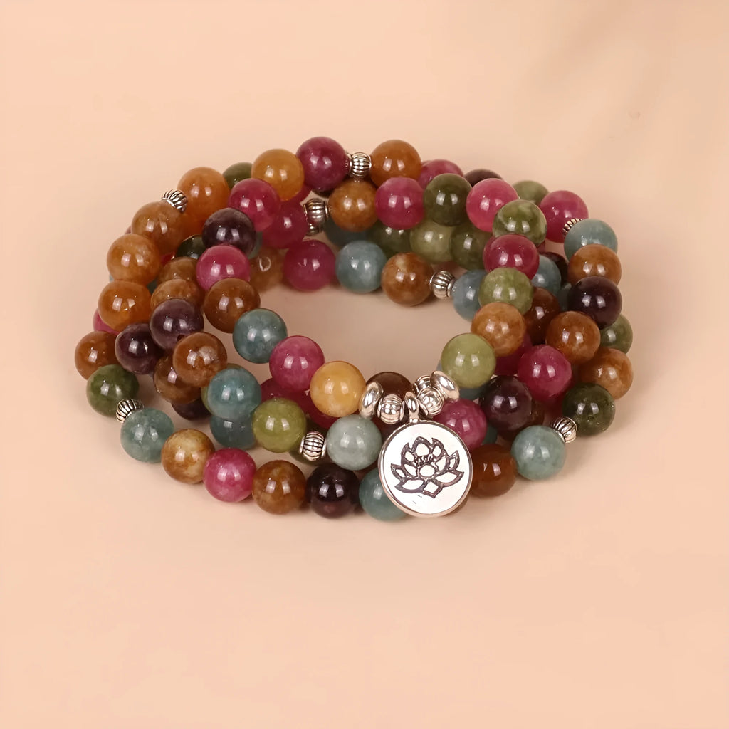 Close-up of a multi-layer beaded bracelet with 108 beads and a hanging lotus charm, made from alloy and tourmaline-coloured material.