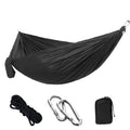 Green and camel parachute cloth double hammock hung between trees with black buckles and ropes.