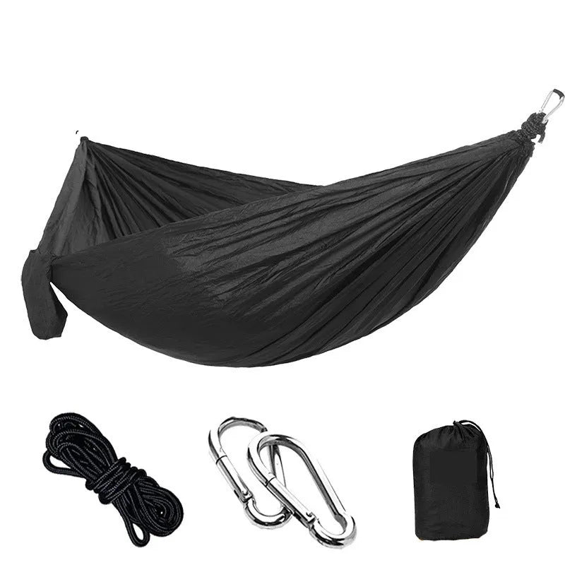 Green and camel parachute cloth double hammock hung between trees with black buckles and ropes.