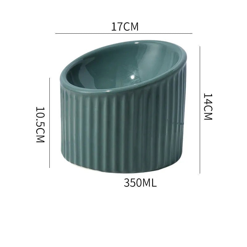 Dark green ceramic elevated cat bowl on a table, showing its raised height and round, tilted shape.