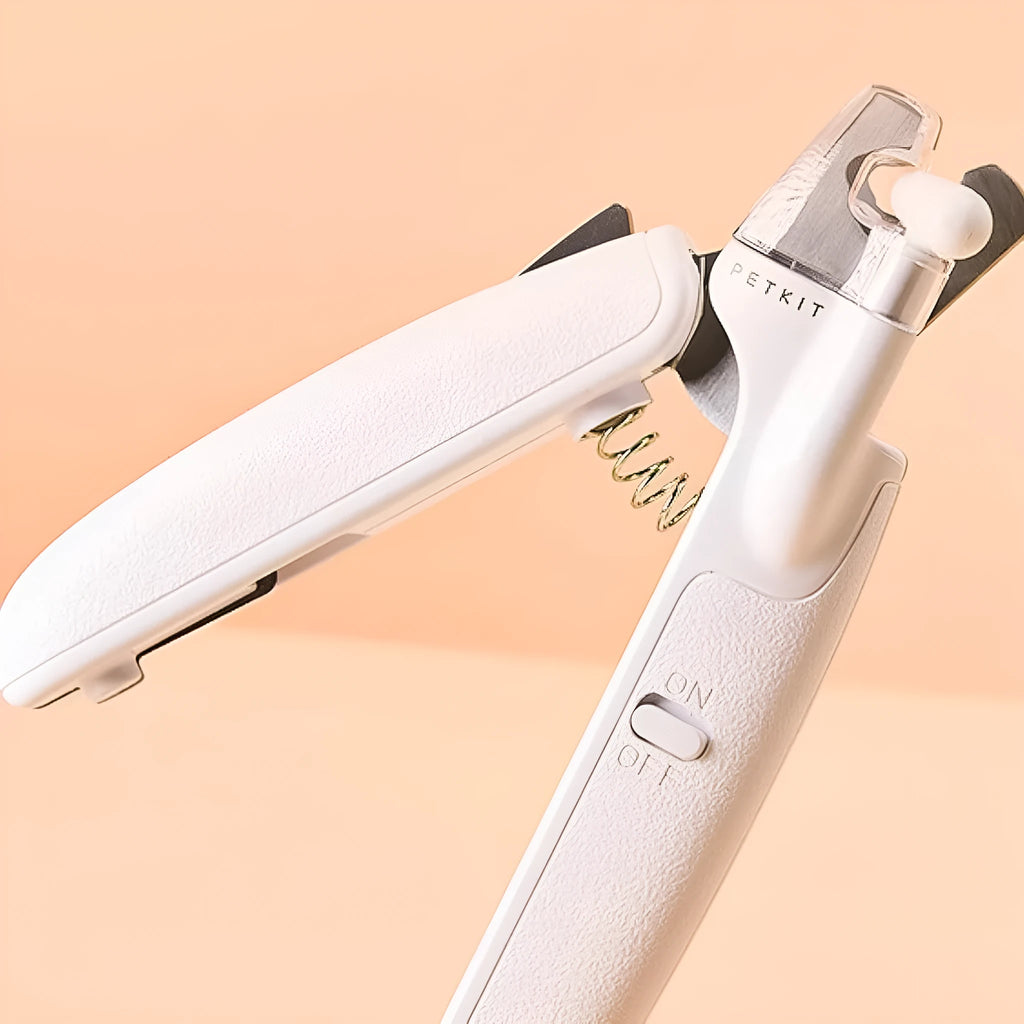 White pet nail clippers with LED light, transparent guard, and leather-like handle next to a nail file.