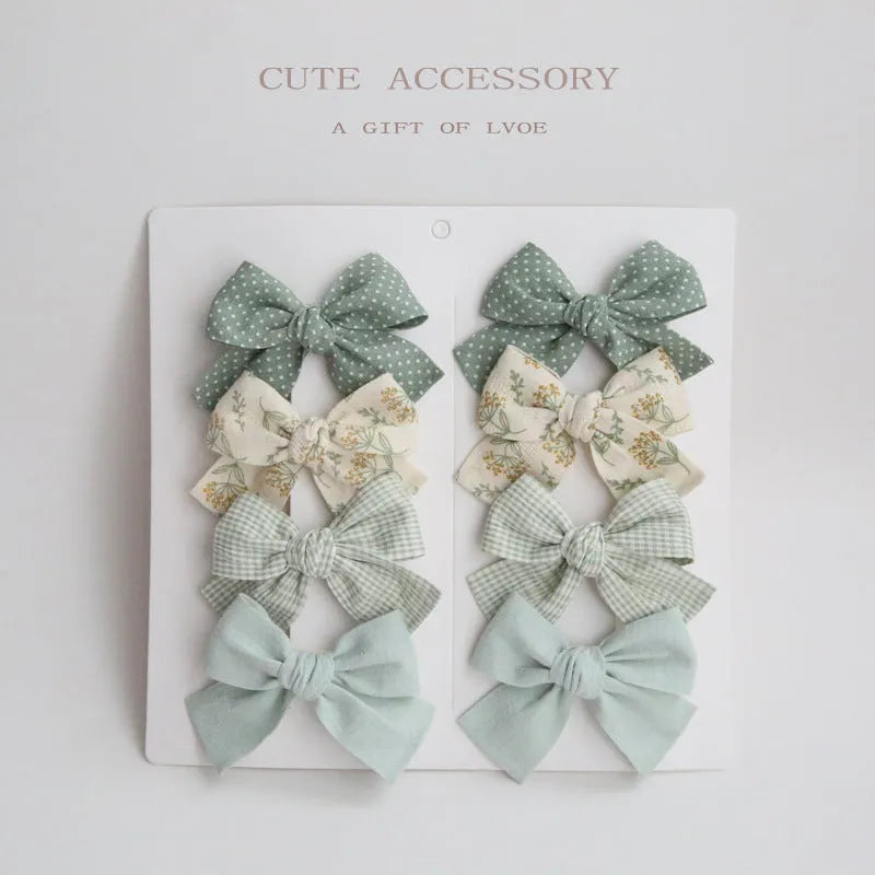 Set of eight children's cloth bow hair clips in various colours including beige polka dot, pink, blue floral, and wine red plaid patterns.