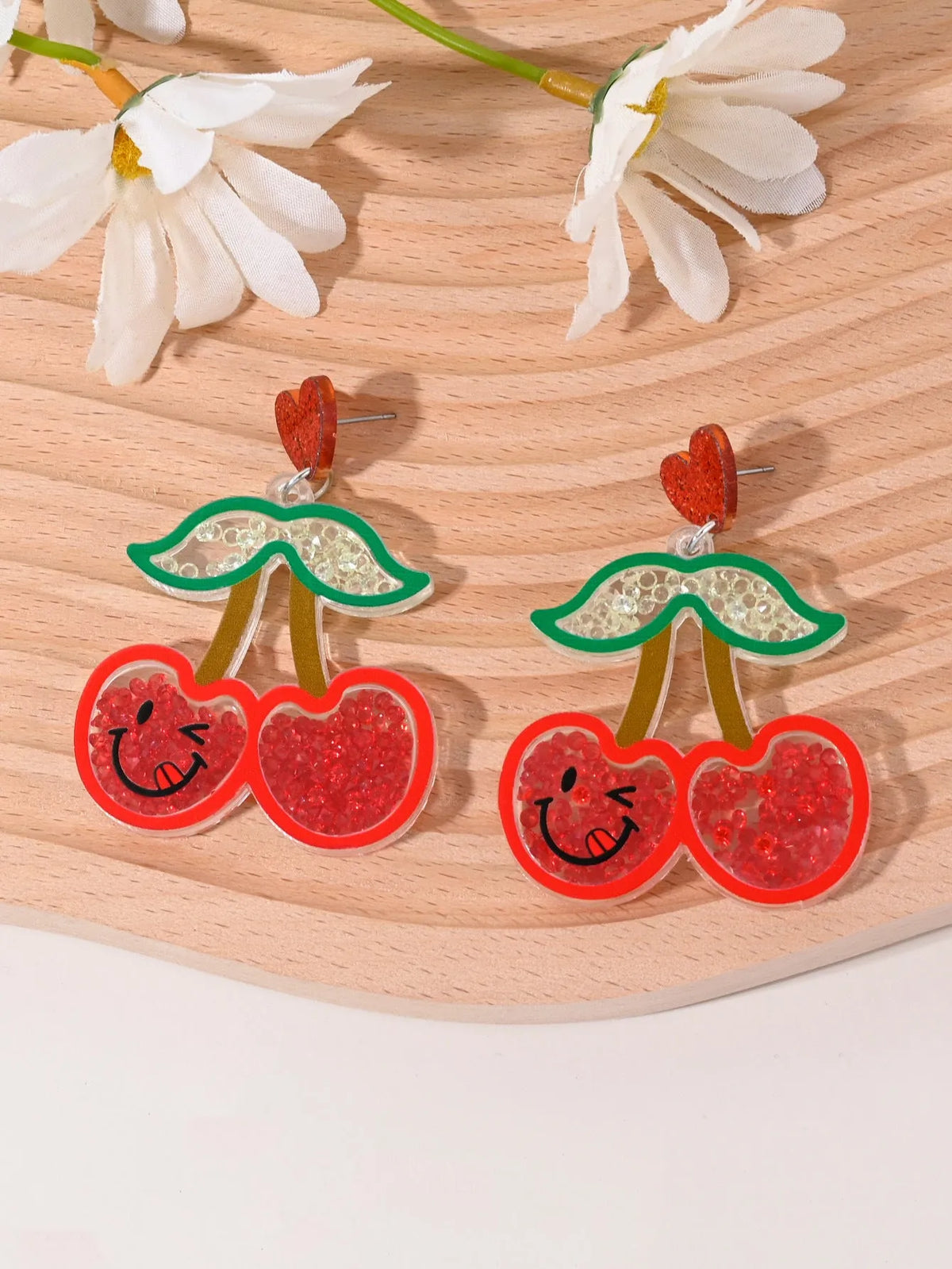 A pair of colourful acrylic earrings with a cake design next to other fruit and ice cream style earrings.