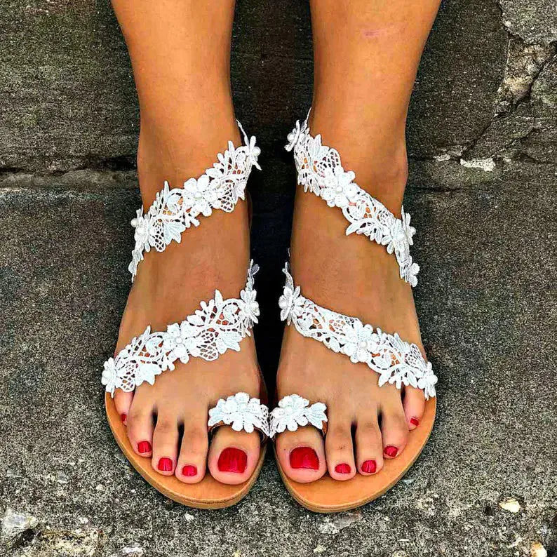 White women's flat sandals with floral pattern and rhinestone decoration on a low slip-on shoe.