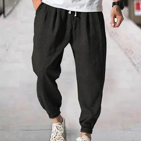 Man modelling loose fit cotton trousers with elasticated ankle cuffs in a light green colour.