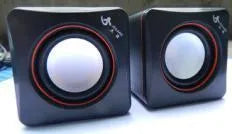 Small black square USB-powered computer speaker with audio and USB cables