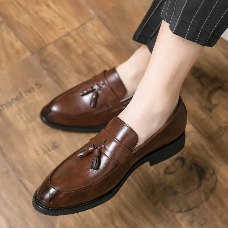 Men's black tassel slip-on loafers with a pointed toe and rubber sole on a white background.