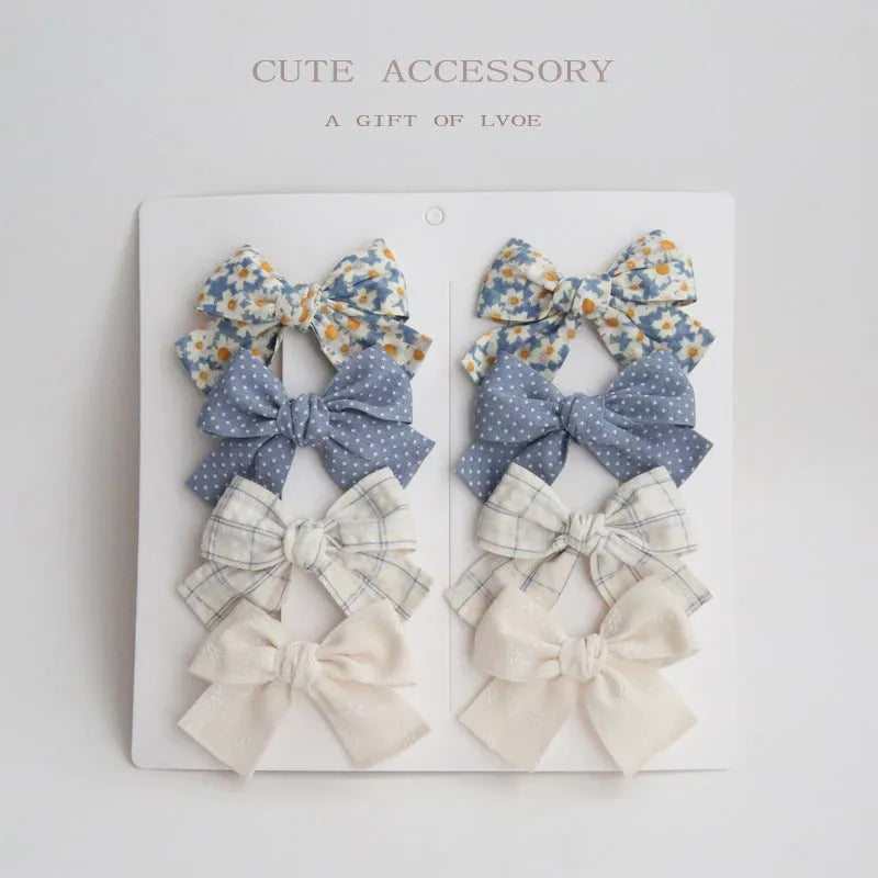 Set of eight children's cloth bow hair clips in various colours including beige polka dot, pink, blue floral, and wine red plaid patterns.
