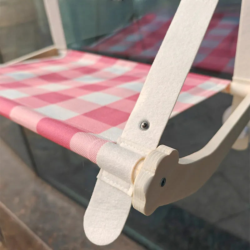 Wooden frame cat hammock with linen mat attached to a window via suction cups, shown in pink colour.