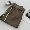 Men's loose straight-leg casual trousers in beige with a drawstring waistband laid flat.