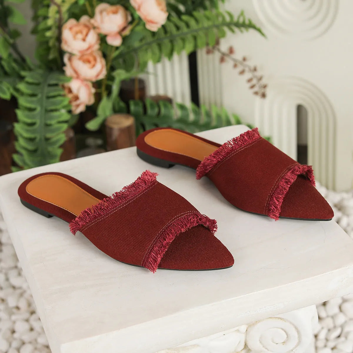 Women's apricot denim flat slippers with tassel detail on a grey background.