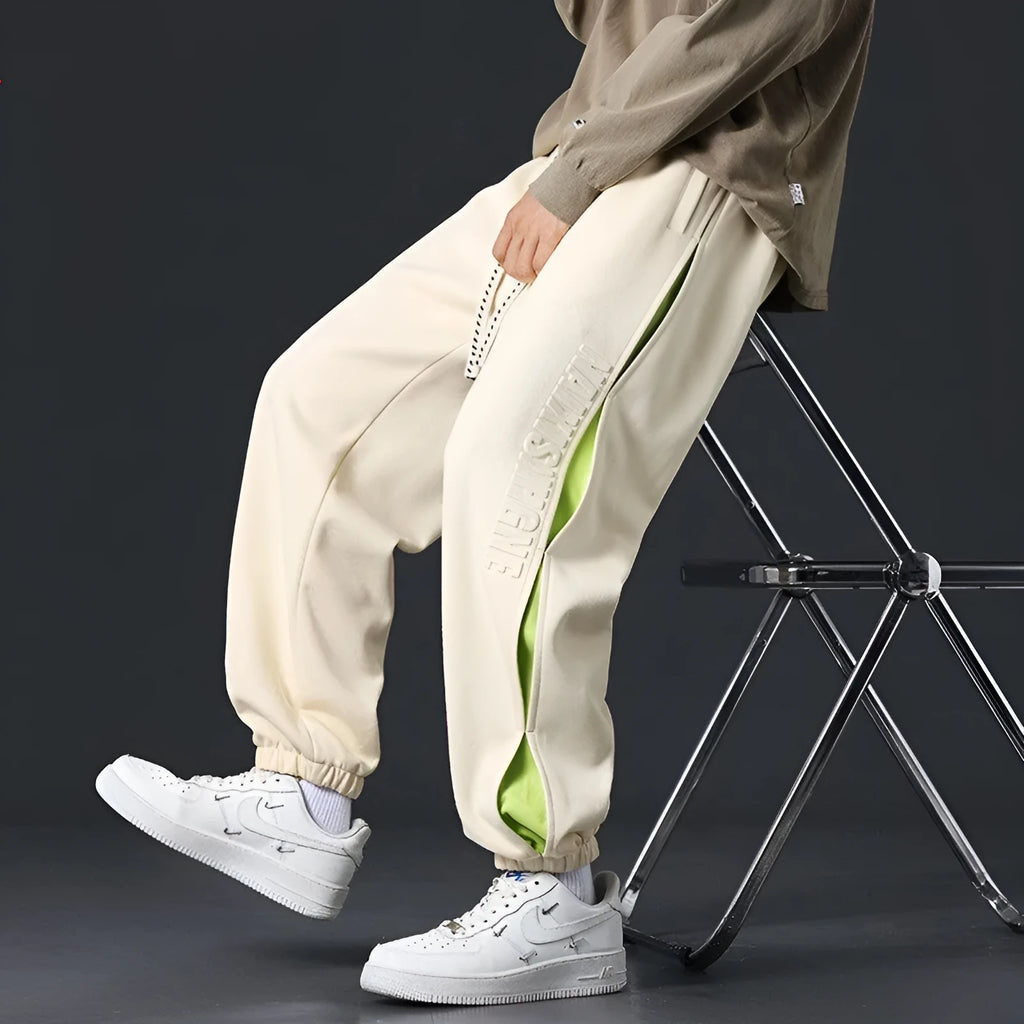 Man wearing grey green loose-fit cotton trousers with stitching print detail and an ankle band.